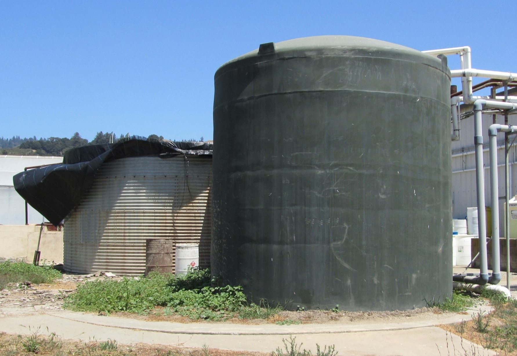 A corrugated slow sand filter tank behind a plastic treated water tank. 