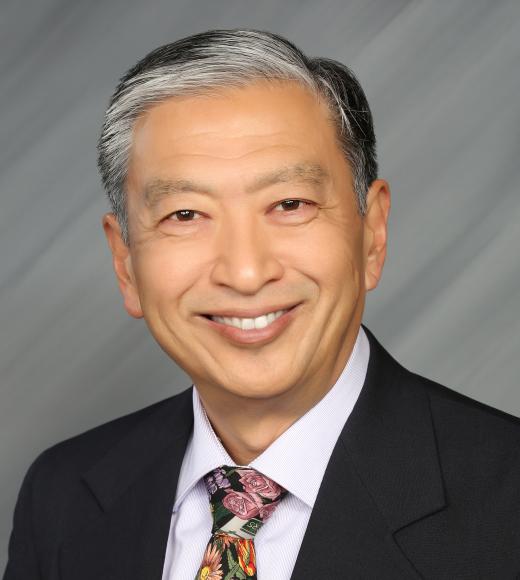 Profile Photo of David Fujino. A photo of a man with black and grey hair smiling and wearing a black suit with a floral tie.