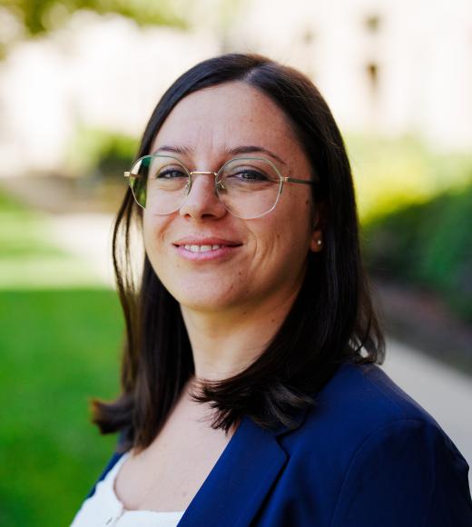 Outdoor professional headshot of smiling woman with glasses and navy blazer